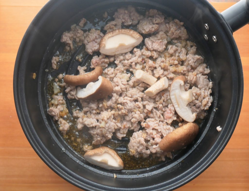 フライ2バディの鍋で炒めたひき肉に、しいたけを加える様子