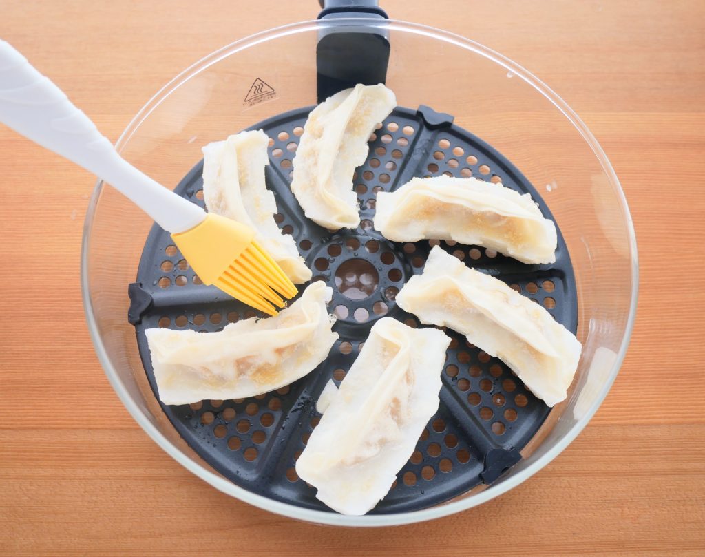 冷凍餃子をガラスポットに並べ、油を塗る様子