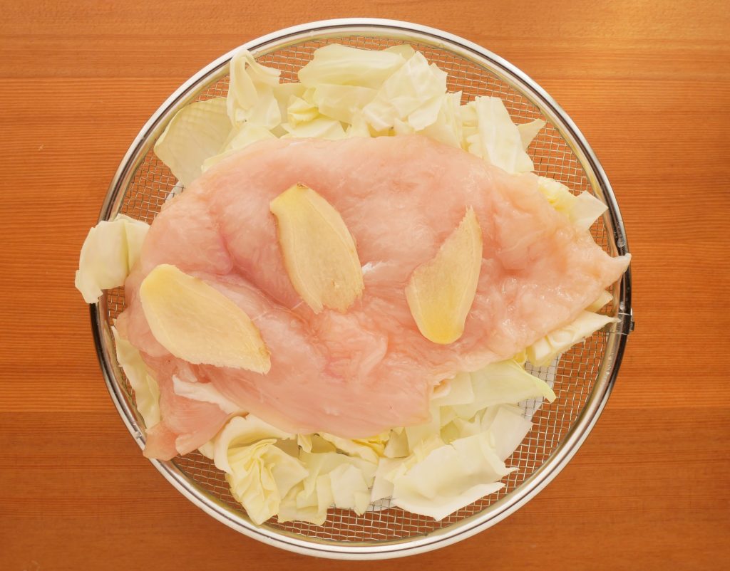 盆ざるに鶏むね肉とキャベツを盛る様子