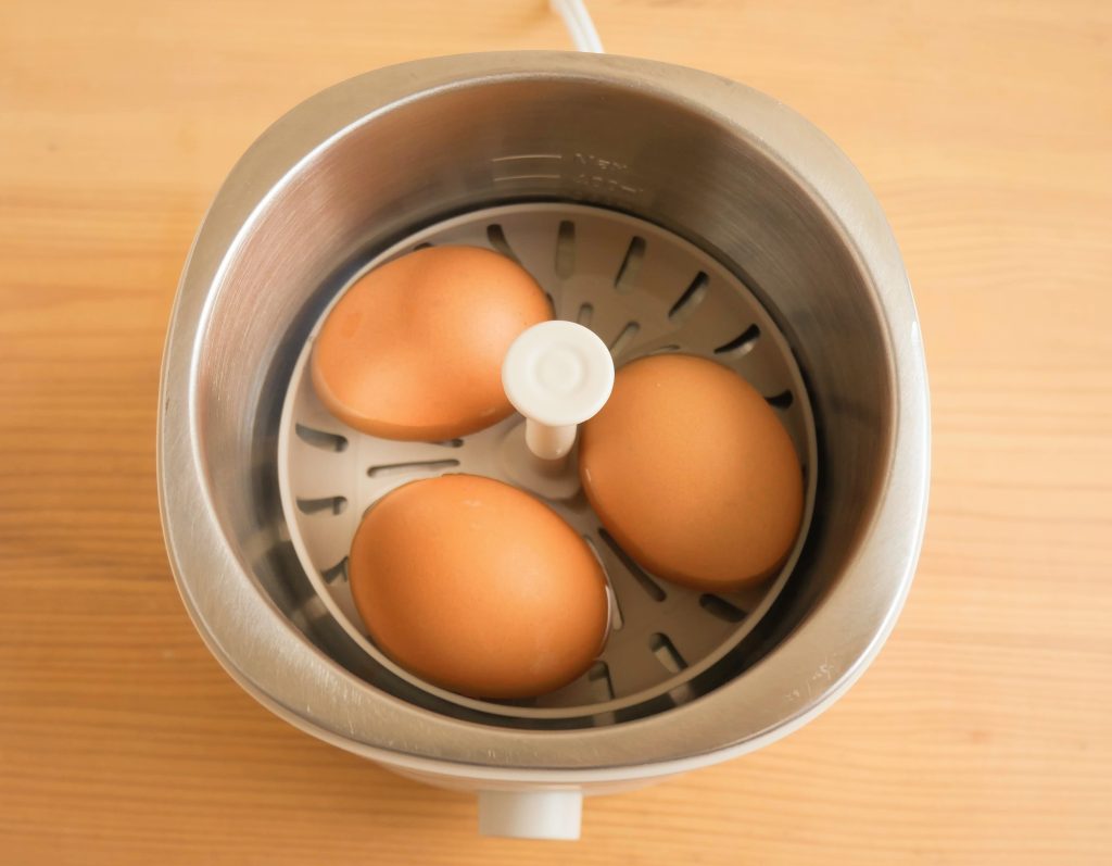 本体に卵をのせたエッグトレイを入れて、水を加える様子