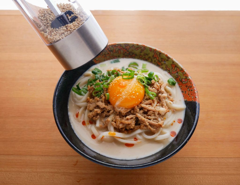 器に盛ったピリ辛ごま豆乳うどんにごまを振りかける様子