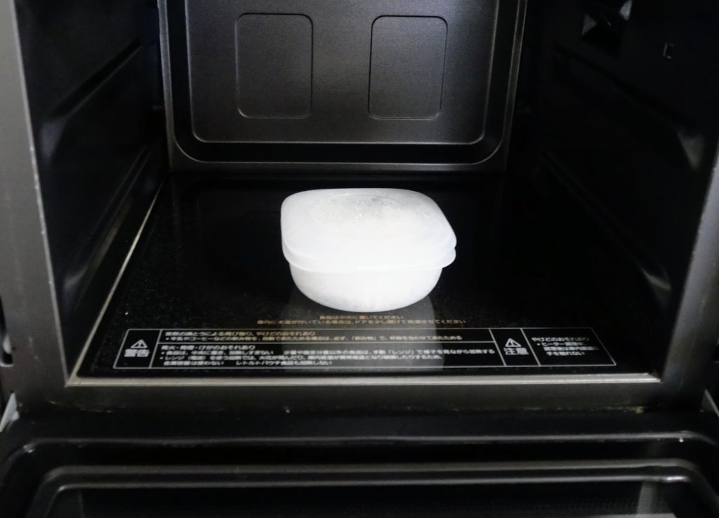 電子レンジに、蒸気であたためる冷凍ごはん容器に入った冷凍ごはんを置く様子