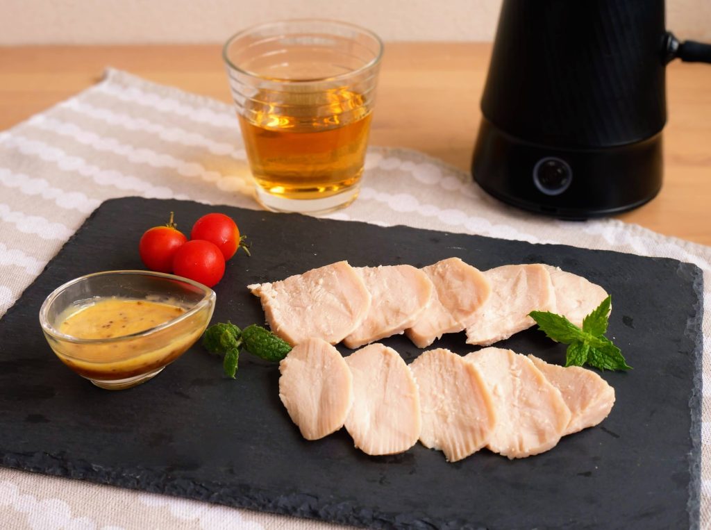 黒い皿にのせてハニーマスタードソースを添えた、燻製サラダチキン
