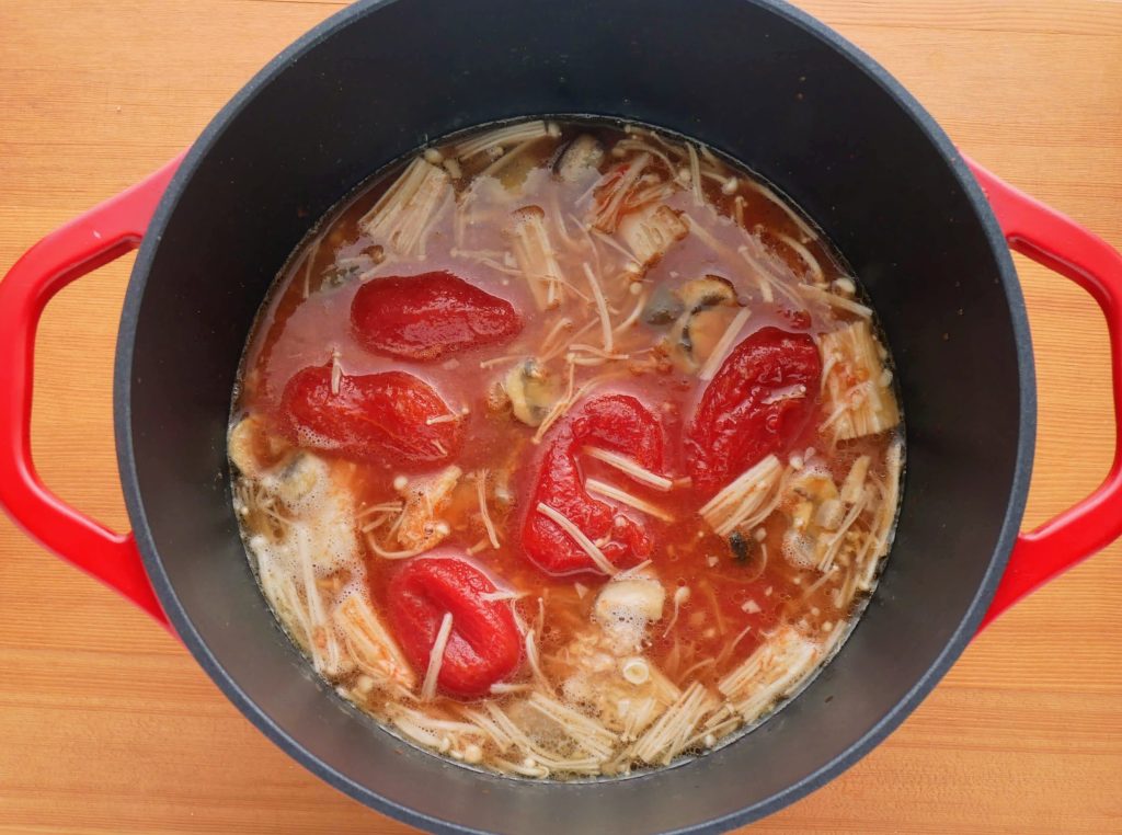 炒めたきのこにトマト缶などの材料を加える様子