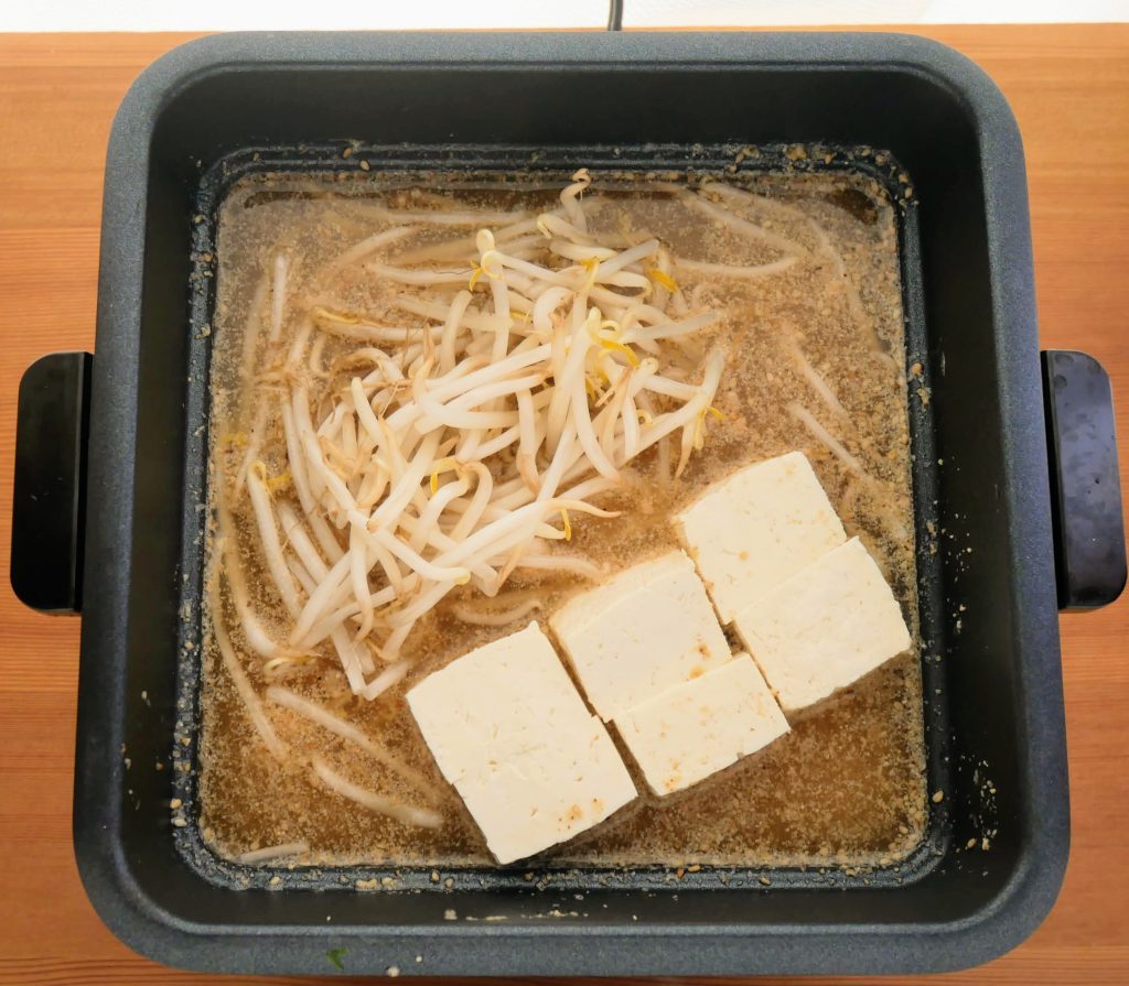 深鍋にスープともやし、豆腐を入れる様子