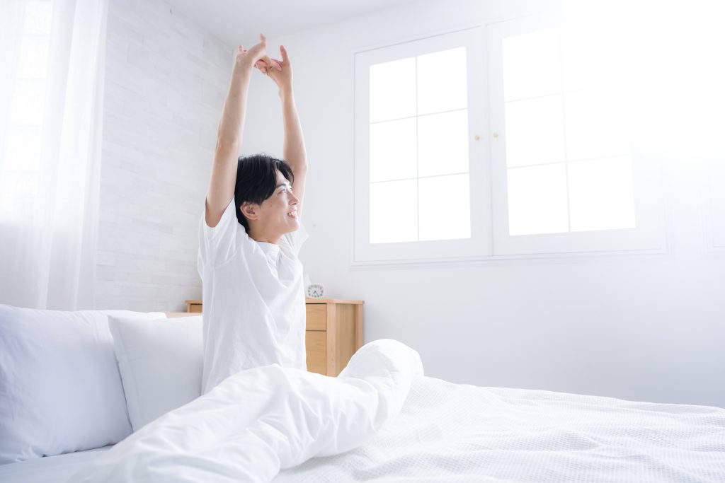 朝、ベッドの上で気持ちよさそうに伸びをする男性