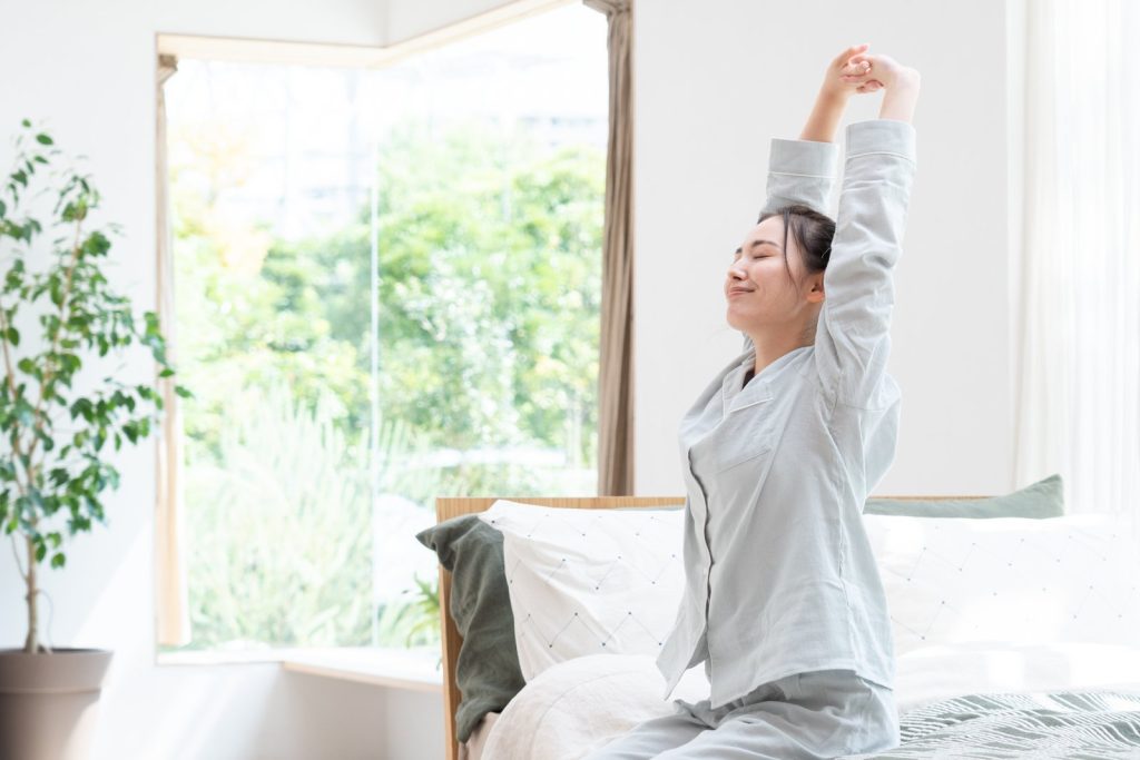 ベットの上で女性が笑顔で伸びをする様子